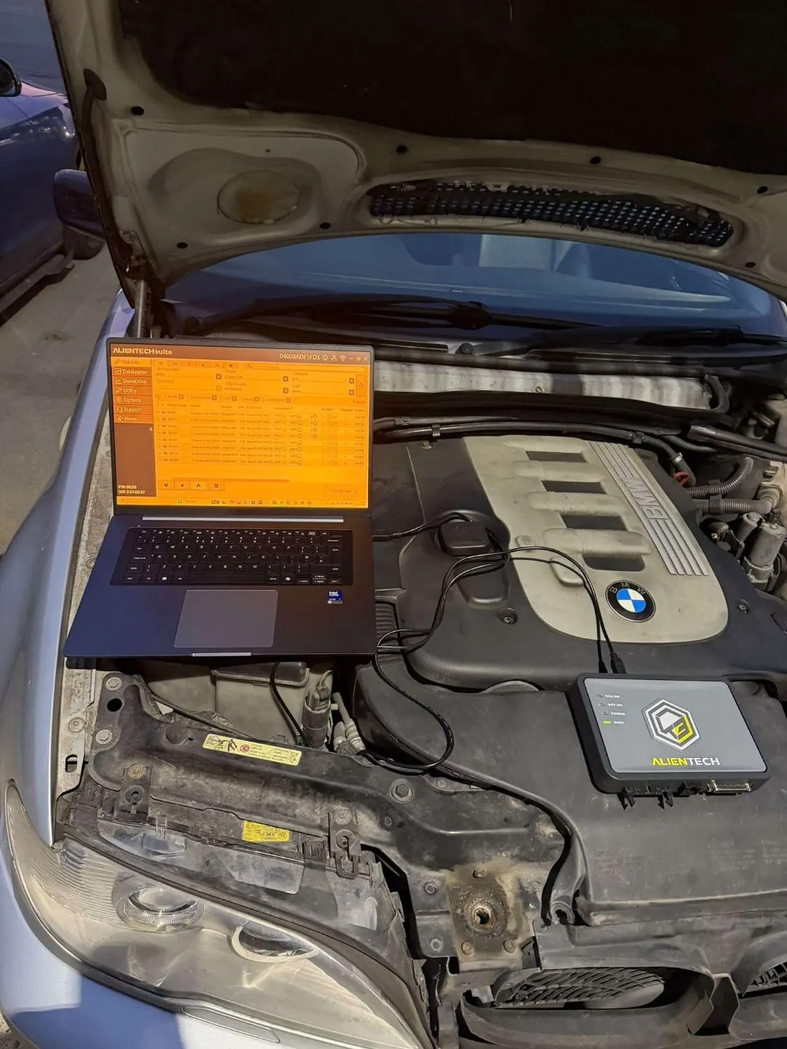 A laptop running tuning software on a BMW six-cylinder diesel, with the remap tool connected beside it