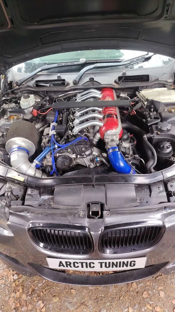A BMW engine bay with a large turbo, polished intake pipes and blue silicone hoses